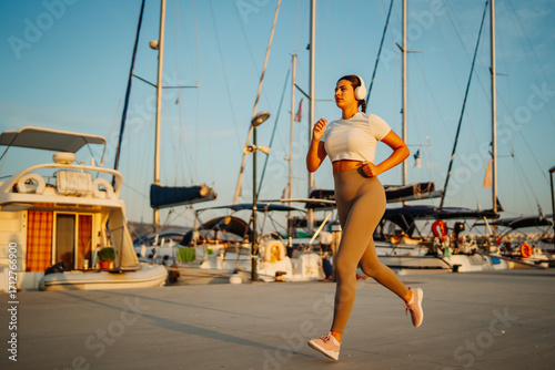 Young caucasian woman running or jogging on the dock by the beach at the sunset