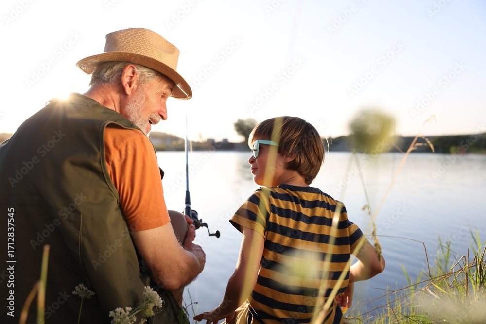 Obraz premium Happy grandfather and his nephew fishing together near river outdoors