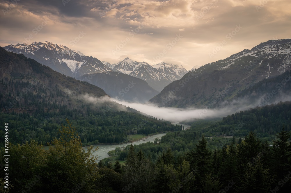 Obraz premium Snow-covered mountain range shrouded in mist under a cloudy sky, evoking a tranquil and enigmatic mood