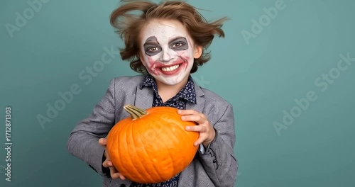 Young boy dressed as the joker with clown makeup holding a pumpkin, celebrating halloween 4k video