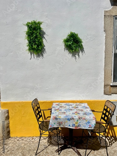 Table avec deux chaises vides et plante sur mur jaune – ambiance méditerranéenne typique