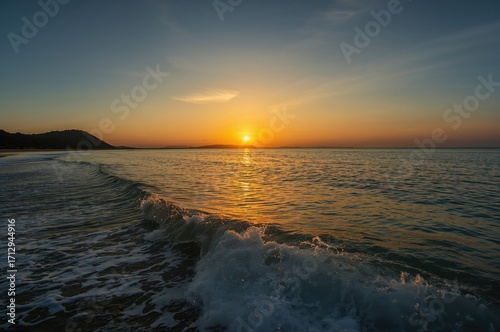 Distant perspective of a seaside at dusk, featuring warm orange and golden hues and gentle vertical waves stirred by a summer breeze.