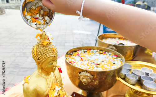 Close up Buddha statue with Hand of sprinkle water onto a Buddha image with leaf. Buddhism ceremony of religion, Believe of Buddhist. Merit and worship. Songkran the most famous festival of Thailand.