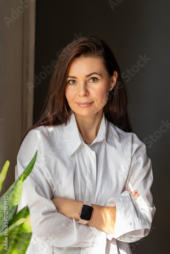Foto Confident woman with long brown hair stands with crossed arms in room