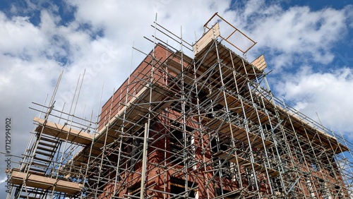 Building under construction covered in scaffolding against a blue sky with clouds, great for illustrating real estate, investment, and development