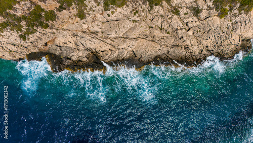 Zakynthos Greece aerial top view of rocky coastline with turquoise Ionian Sea waves splashing against sharp stone cliffs in summer sunlight