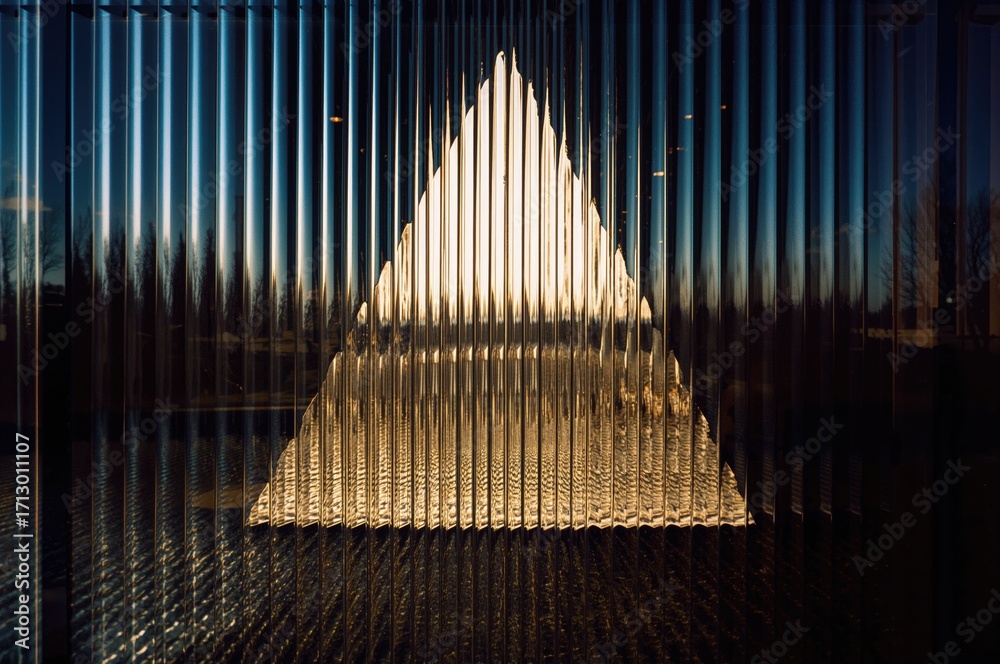 Obraz premium View through textured glass distorting the external scenery with combined light reflections and refractions forming triangular shadows and highlights.