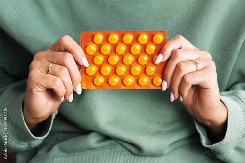 Female hands holding blister pack with orange pills. Pharmacy medicine packaging closeup. Vitamins and supplements for health treatment. Healthcare and medical concept. Pharmaceutical background.