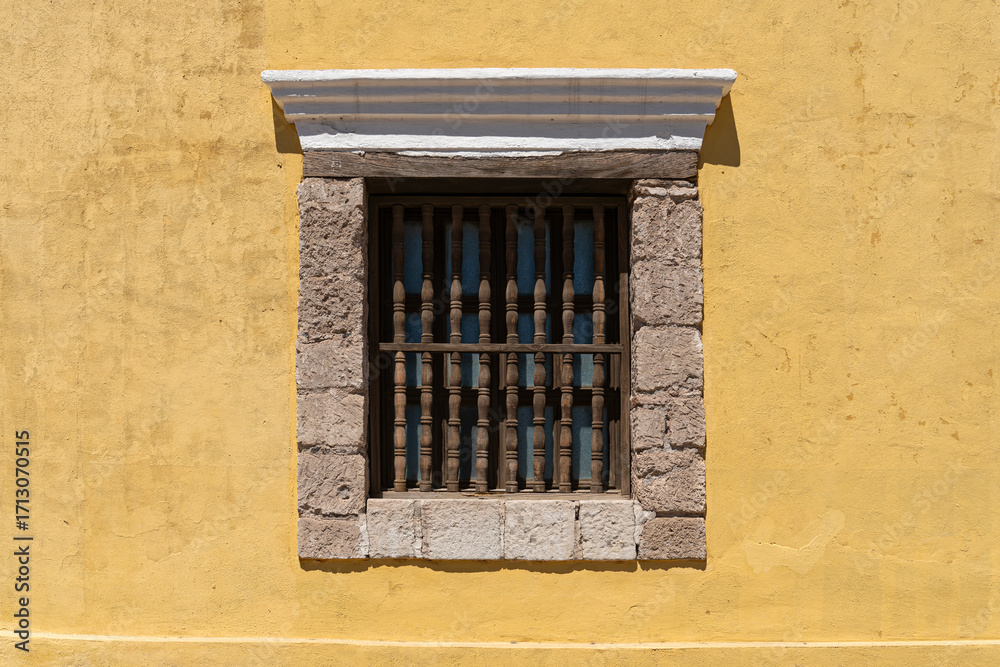 Fototapeta premium stone framed window with wooden bars in a yellow stucco building