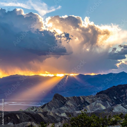 Dramatic sunset illuminates colorful mountain ranges, piercing through a dramatic sky full of clouds.