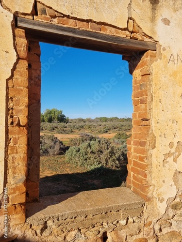 View through the window of ruins of a stone building overlooking the Australian outback. A blue sky over desert and saltbush plants. Taken near Silverton in New South Wales