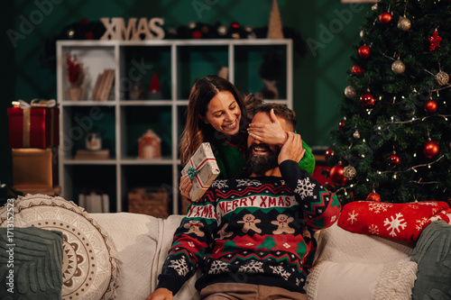 Fotografie Woman surprising her boyfriend with christmas gift at home