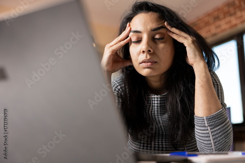 Valokuva Fatigued indian woman seated at desk with eyes closed, taking break and massaging her temples
