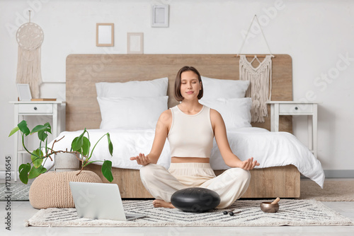 Beautiful young woman with glucophone meditating on carpet in bedroom