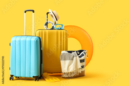 Suitcases with inflatable ring, summer bag and beach accessories on yellow background. Vacation concept