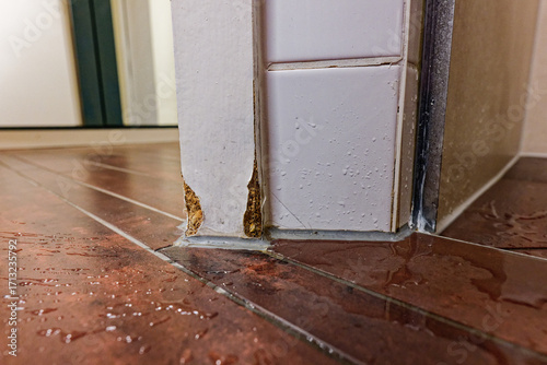 Wet wooden floor with splashes door ajar and swollen panel