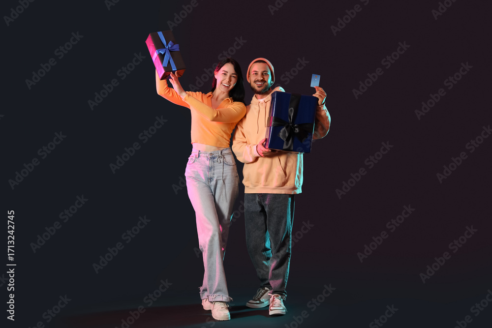 Fototapeta premium Young couple with credit card and gifts on dark background. Cyber Monday