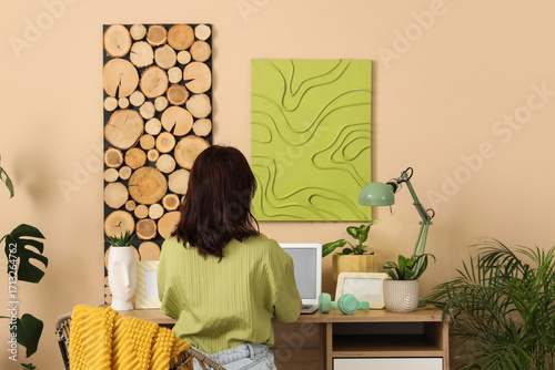 Young woman working with laptop and houseplants at desk in office, back view