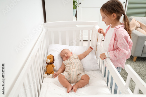 Little girl and her sleeping baby brother in crib at home