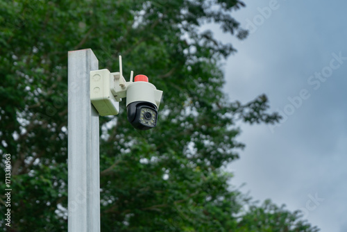 CCTV camera installed on the top of a pole at the outdoor location have a large tree as a background with space of sky
