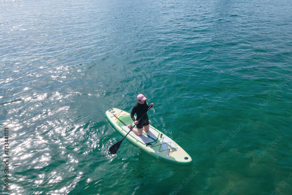 Fototapeta premium Young woman sitting on sup board and holding an oar at sea.