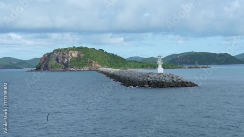 Rocky island breakwater lighthouse blue sea green hill cloudy sky peaceful nature tropical landscape, tranquil scene with rocky breakwater leading to small white lighthouse, lush green island