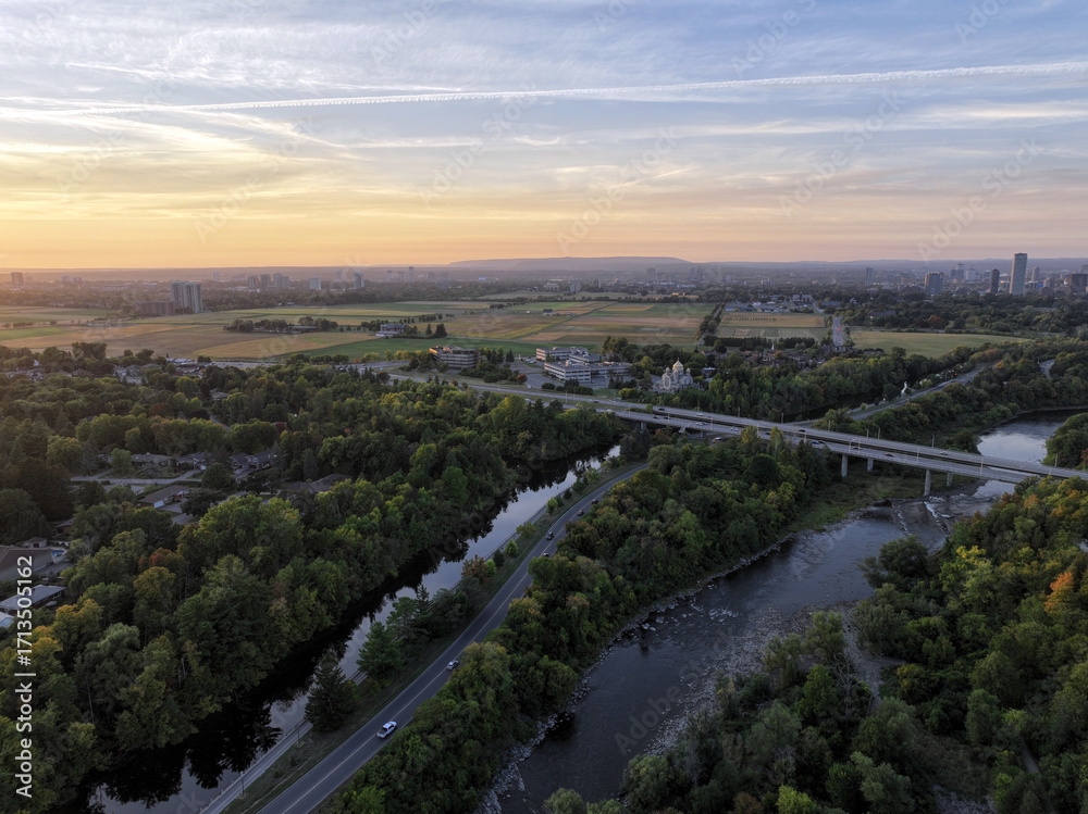 Fototapeta premium Aerial view of a winding river flowing through a forested landscape with a bridge and a distant city on the horizon