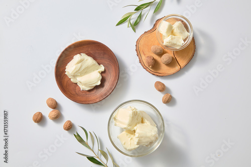 Papier peint Simple overhead layout with glass jar of shea butter, whole nuts, wooden dish and olive twig against white background for natural skincare ingredient themes