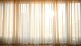 Elegant sheer curtains softly draped over a large window, sunlight streaming through,   window dressing,   interior design