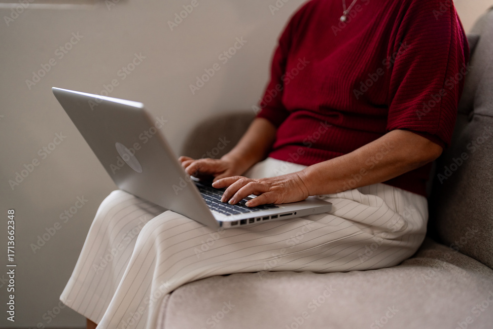 Naklejka premium Older Asian woman remote working from home learning new skills online Senior adult using computer on sofa at apartment Digital literacy for elders