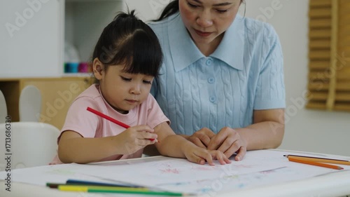 toddler baby girl training to drawing with colored pencil with mother helping on a desk at home