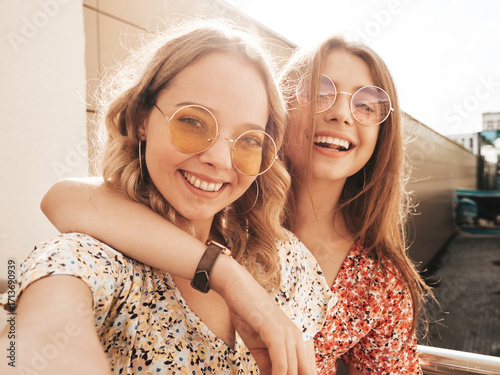 Two young beautiful smiling hipster female in trendy summer sundress.Sexy carefree women posing on the street background. Positive models having fun