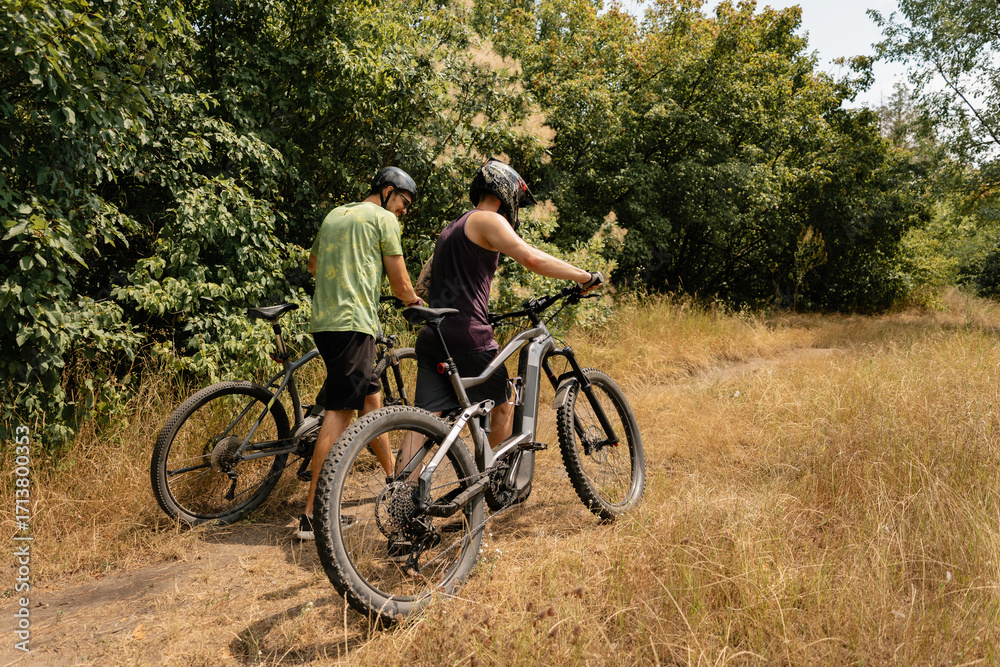 Naklejka premium Two cyclists with MTB bikes pause on a trail surrounded by green forest scenery
