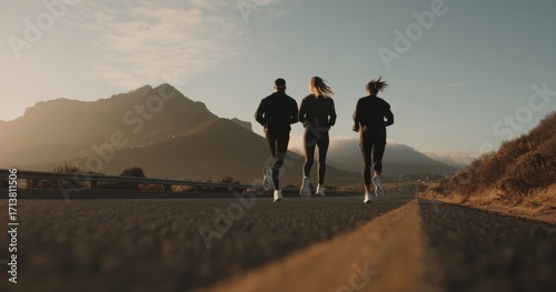 A Group of Three Runners Enjoying a Scenic Jog Along a Coastal Road with Majestic Mountains in the Background During Sunrise