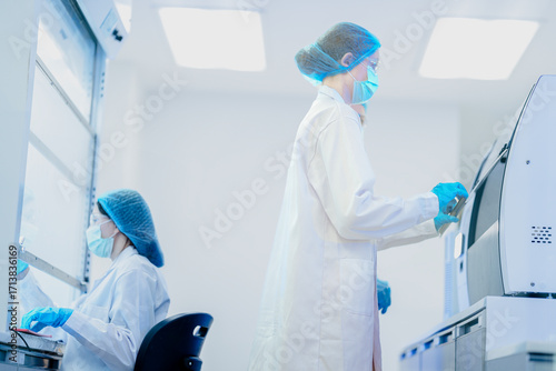 A researcher performs an aseptic technique inside a Class II biosafety cabinet. The sterile environment is critical for cell culture or virology work in a biotechnology lab.