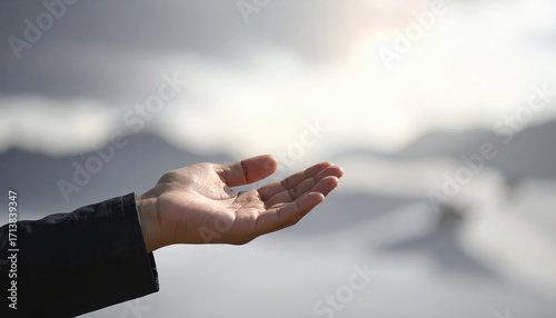 An outstretched hand reaches out to the softly lit sky, a gesture of openness and hope against a blurred backdrop of misty mountains.