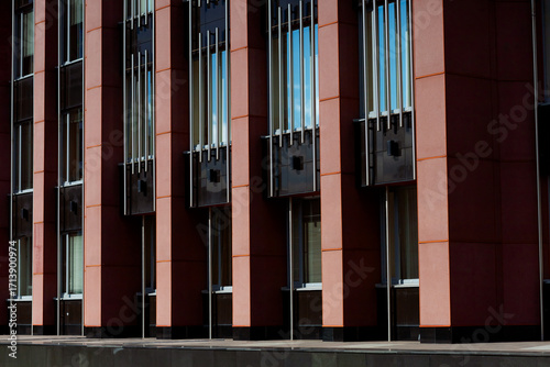 The building's façade features a contemporary style with vertical elements. Red panels alternate with large windows, creating a clean and minimalist look. Metal inserts add dynamism and accents.