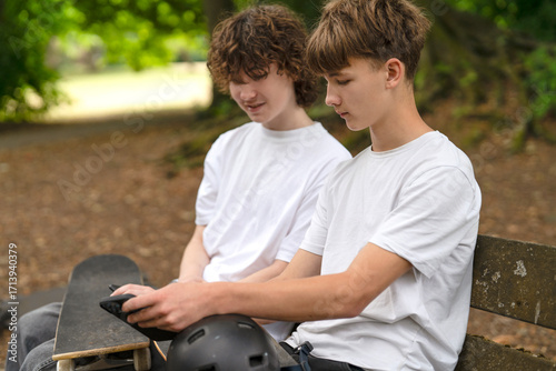 Tapeta Two boys enjoy downtime at a skate park, discussing tricks and checking equipmen