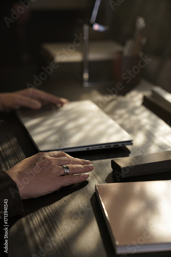 Φωτογραφία Close-up of man’s hands closing laptop at office desk under warm sunlight, symbolizing end of workday or business pause