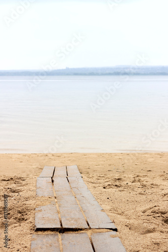 A path made of wooden beams on a sandy beach leading to a river in cloudy weather