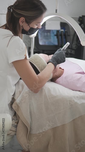 Vertical video of a cosmetologist performing a professional microneedling facial treatment on a woman at a beauty salon