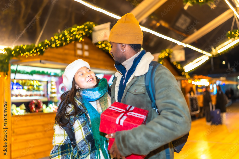 Fototapeta premium Happy multiethnic couple holding christmas gift at christmas market