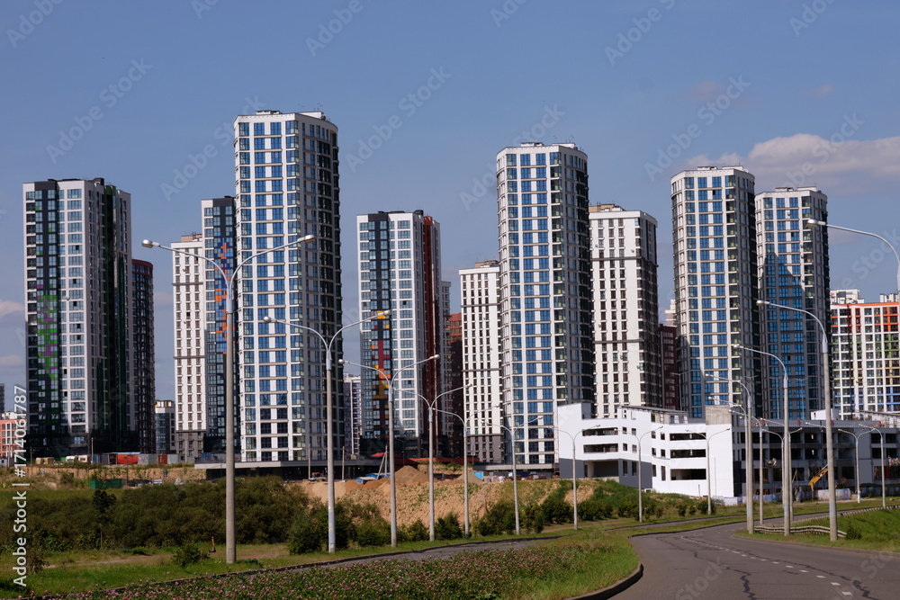 Obraz premium Newly constructed skyscrapers rise tall against a stunning blue sky, showcasing sleek architecture in a rapidly developing city. Greenery adds contrast to the urban scene
