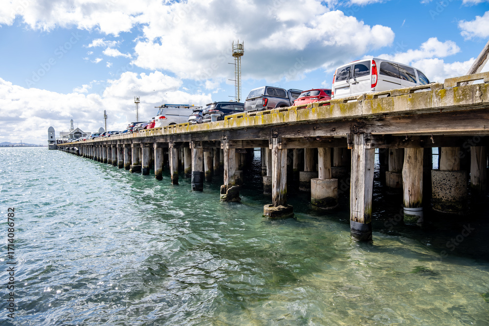 Obraz premium Cunningham Pier in Geelong, Victoria, Australia, with parked cars above wooden pylons over blue coastal waters. Concept of historic pier, maritime infrastructure, waterfront tourism