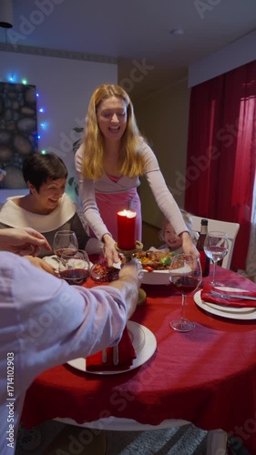Family Christmas dinner at home. Woman serving roast turkey with vegetables on festive holiday table with candles, wine glasses, and happy relatives. Warm cozy atmosphere of winter celebration