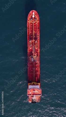 Top-down aerial video of a red oil tanker ship floating in the open sea. Industrial marine vessel captured in bright daylight, showing deck structures and equipment in detail