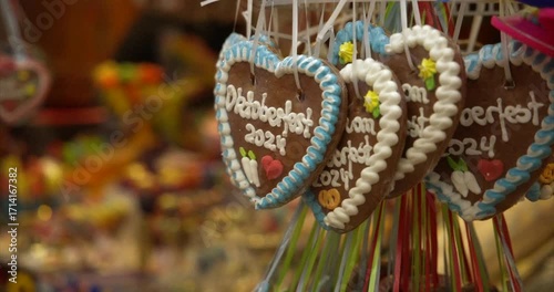 Oktoberfest cookie heart with blurred background shows traditional German celebration. Oktoberfest cookie detail includes white icing and hanging decoration, moving camera
