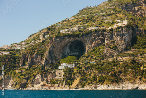 Scenic view of the Emerald Grotto (Grotta dello Smeraldo) on the Amalfi Coast, Italy. Large natural cave in limestone cliffs with Mediterranean landscape and coastal village houses above. 