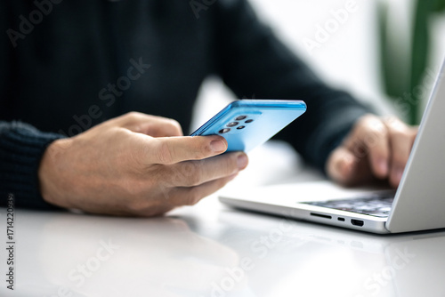 Closeup image of a male hands using smartphone and laptop. Boy working online, internet applications