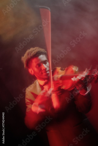 Black young adult man playing violin on stage, wearing suit, captured in motion with blurred effect, focused expression, dramatic lighting, performing classical music